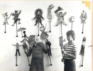 vor einer Wand stehen Kinder mit Stabpuppen, schwarz-weiß-Foto