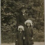 schwarz-weiß-Fotografie von einer Frau mit zwei Mkleinen Mädchen, die eine Haube tragen