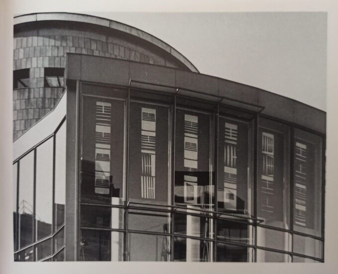 Die Fotografie stellt die Fassade der Schirn Kunstalle 1991 versehen mit eine fotografische Installation von der Künstlerin Irene Peschick. Dabei handelt es sich um große Fahnen mit Streifen, die an den Fenster von der Innenseite der Gebäude aufgehängt sind.