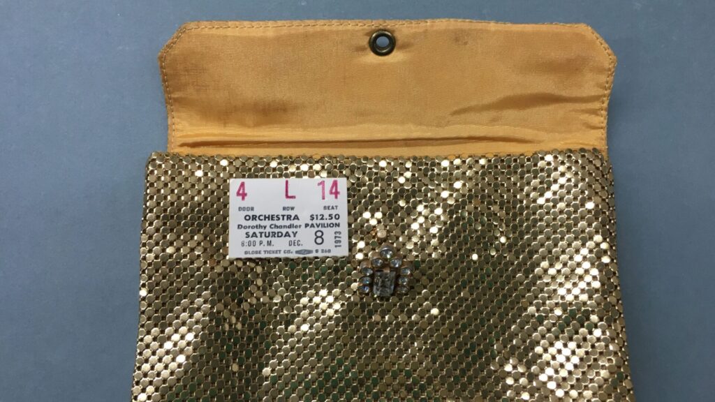 mit goldenen Pailletten besetzte handtasche, auf der eine Eintrittskarte von 1975 liegt