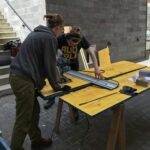 zwei Personen arbeiten an einem gelben Tisch