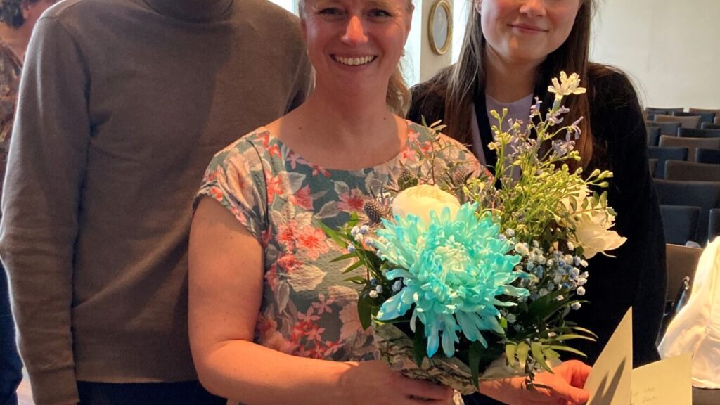 eine Frau mit einem Blumenstrauß, hinter ihr stehen ein Mann und eine Frau