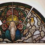 Ein halbrundes Glasgemälde zeigt eine Darstellung Gott Vaters mit ausgebreiteten Armen. Vier weitere darum herum angeordnete Scheiben bilden den Hintergrund der Darstellung in Form bunter Ornamente.