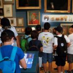 Kinder stehen vor eine Ausstellungswand mit vielen Bildern